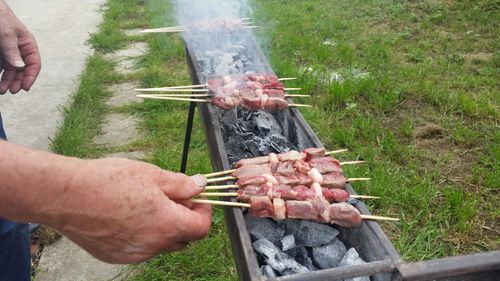 Cropped image of man preparing roasting meat skewers at yard