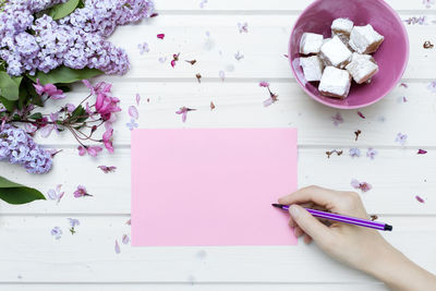 Cropped hand of woman writing on paper with objects on table