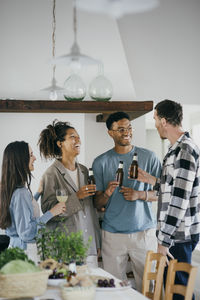Happy friends holding alcoholic drinks while talking during dinner party at home