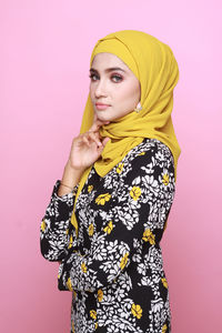 Portrait of young woman standing against pink background