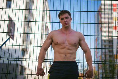 Portrait of muscular man standing against fence at park