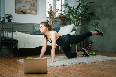 Positive athletic woman with neatly tied hair and tight sportswear doing performs lying kicks 