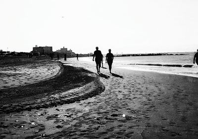 People walking on beach against clear sky