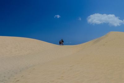 Man riding motorcycle in desert against blue sky