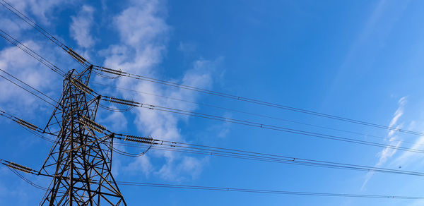 Low angle view of electricity pylon against blue sky