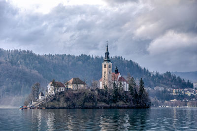 Buildings by river against cloudy sky