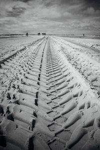 Surface level of tire tracks on sand at beach against sky