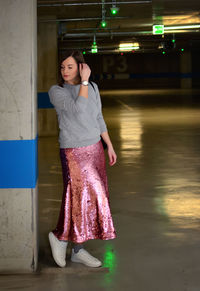 Full length of young woman looking away while standing at parking lot