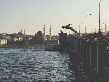 People on river by city against clear sky