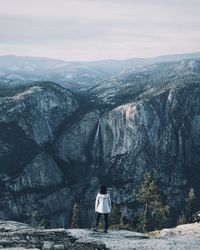 Rear view of woman standing on rock against sky