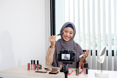 Young woman blogging while applying make up at office