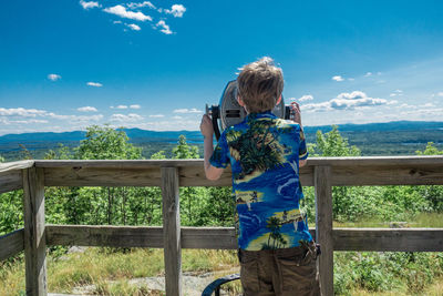 Boy standing by railing against sea and blue sky