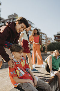 Playful boys with female friends siting on wall at street