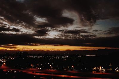 View of illuminated city against cloudy sky at sunset