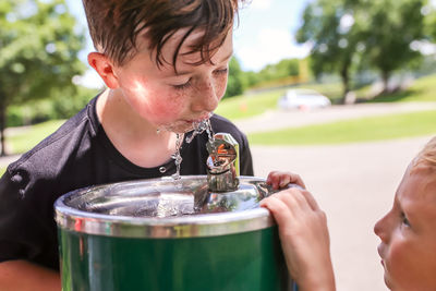 Close-up of boy drinking water from fountain while brother looking