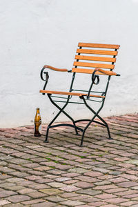 Empty bench on footpath against wall