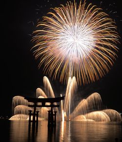 Silhouette torii gate in lake against firework display at night