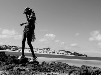 Full length of woman standing on rock at beach against sky