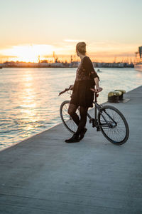 Rear view of man riding bicycle on riverbank