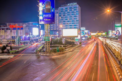 Light trails on road amidst buildings against sky at night