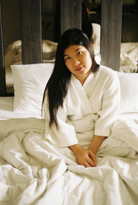 Portrait of young woman sitting on bed at home