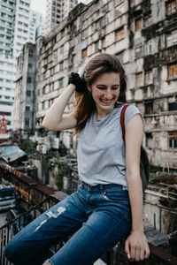 Smiling young woman sitting on railing against building