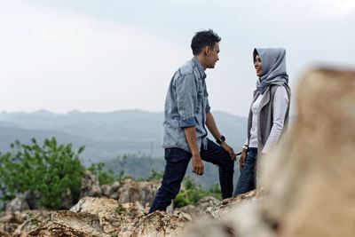 Side view of couple standing on rocks against sky