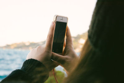 Close-up of hand using mobile phone against sky