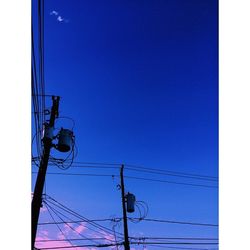 Low angle view of electricity pylon against blue sky