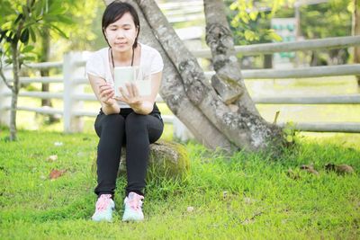 Portrait of woman sitting on grass against trees