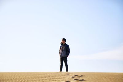 Full length of man standing on sand dune against sky