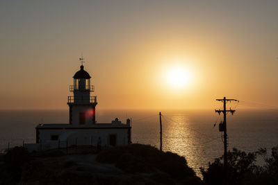 Lighthouse by sea against sky during sunset