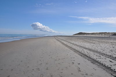 Tire tracks and footprints on beach against cloudy sky