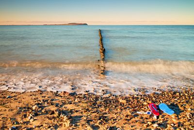 Blue red flip flops and white swimming goggles ready for using on stony beach at wooden breakwater. 