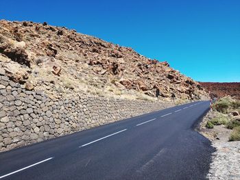 Road by mountain against clear blue sky