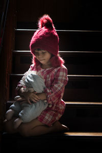 Cute girl holding stuffed toy sitting on staircase at home