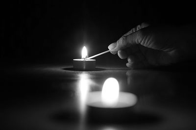 Cropped hand lighting tea light candle in darkroom