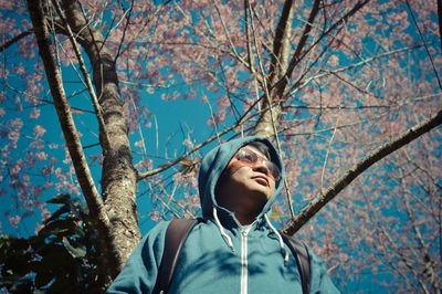 Low angle view of man wearing sunglasses standing against tree