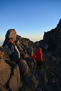 Rear view of people on rock formation against clear sky