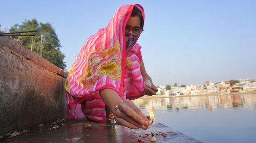 Woman sitting by river against sky