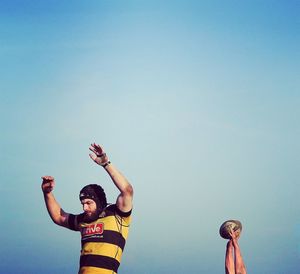 Man playing rugby with friend against clear blue sky