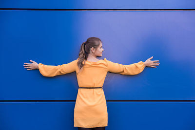 Woman with arms outstretched standing against blue wall