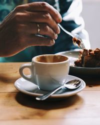 Midsection of man eating cake while having coffee