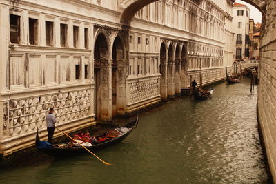 Man standing on gondola by building at grand canal in city