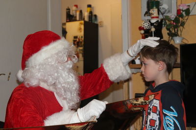 Man wearing santa claus costume touching boy at home