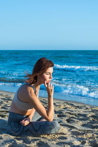 Young woman sitting on shore at beach against clear sky