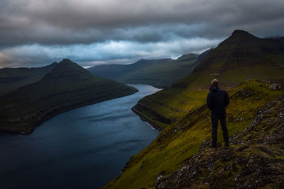 Hiker standing on mountain against cloudy sky during sunset