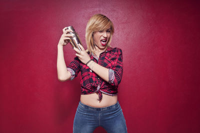 Portrait of barmaid shaking cocktail against red wall