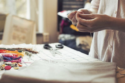 Midsection of woman threading needle at table