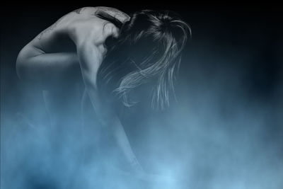 Naked woman amidst smoke against black background